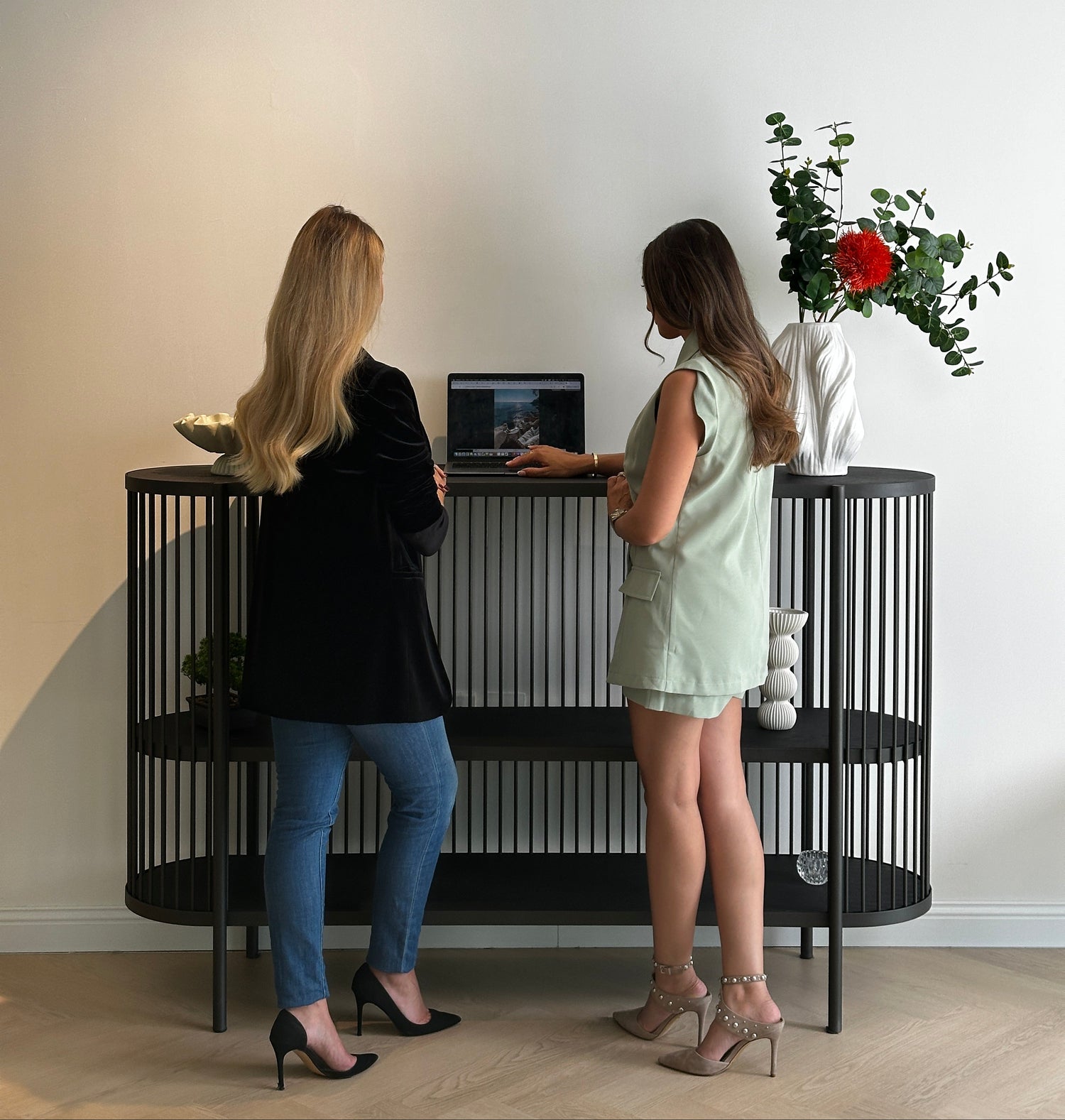 Two women sitting on a bench with a vase of flowers above them